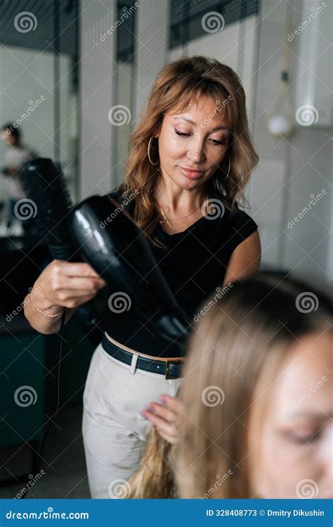 Vertical Portrait Of Professional Female Hairdresser Drying And Straightening Long Blonde Client