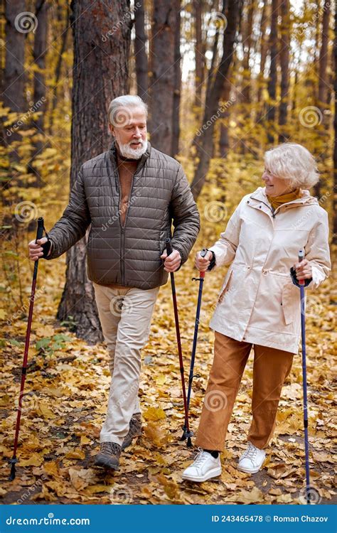 Senior Couple Walking With Nordic Walking Poles In Autumn Park Mature