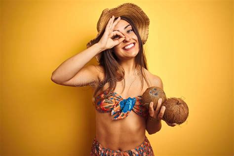 Mujer De Vacaciones Vistiendo Bikini Y Sombrero Sosteniendo Coco Sobre Fondo Amarillo Aislado