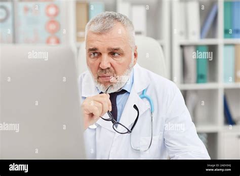 Mature Doctor Sitting In Front Of Computer Monitor And Thinking About