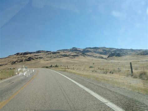 An Open Road With Mountains In The Background And Grass On Both Sides