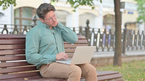 Mature Adult Man Having Neck Pain While Using Laptop On Bench Stock