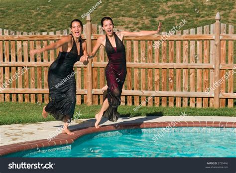 Two Young Women In Formal Dresses Running And Jumping Into A Pool