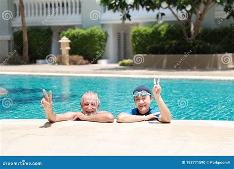 Happy Elderly Caucasian Husband And Elderly Asian Wife Take A Break While Swimming In Pool