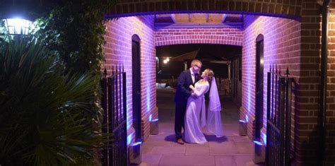 a bride and groom standing in front of a brick archway at night with purple lighting