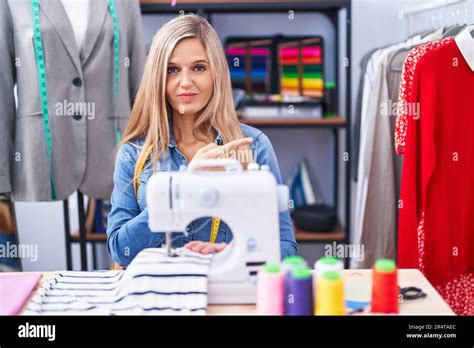 Blonde Woman Dressmaker Designer Using Sew Machine Pointing With Hand Finger To The Side Showing