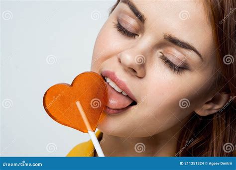 Cheerful Pretty Woman Licking Heart Shaped Lollipop Close Up Studio