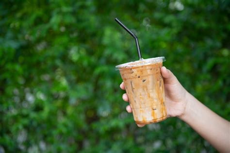 Premium Photo Woman Hand Holding The Glass Iced Coffee On Fresh Coffee Beans In Coffee Plants Tree