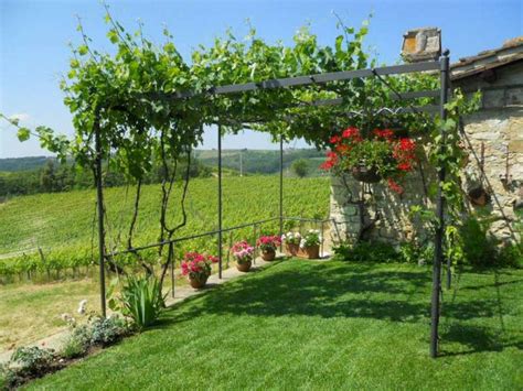 A Red Table Sitting Under A Trellis Next To A Lush Green Field