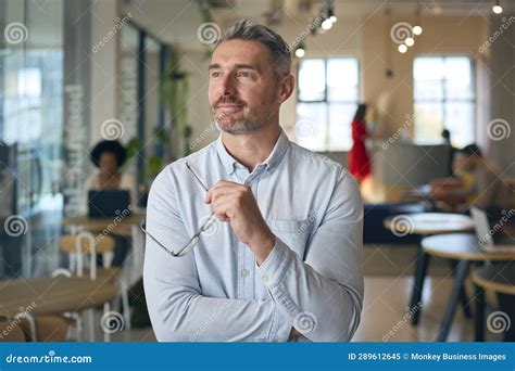 Portrait Of Smiling Mature Businessman Holding Glasses Standing In Busy