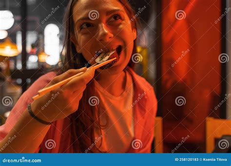 Portrait Of Smiling Brunette Woman Eating Sushi Rolls With Chopsticks And Enjoying The Taste