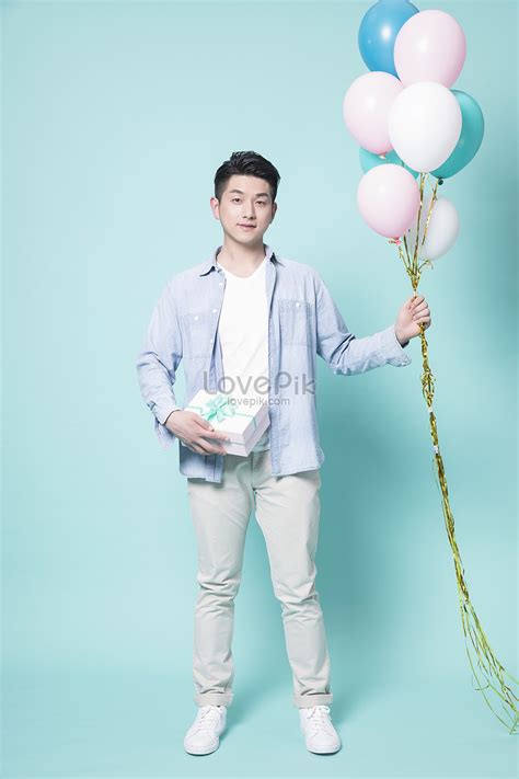 Varón Joven Que Sostiene Un Globo Que Da Un Rectángulo De Regalo Foto