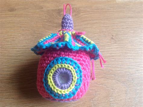 A Crocheted Camera Ornament Hanging On A Wooden Table With Pink Blue