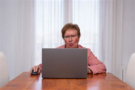 Wanita Senior Dengan Ekspresi Ragu Menggunakan Laptop Di Rumah Foto