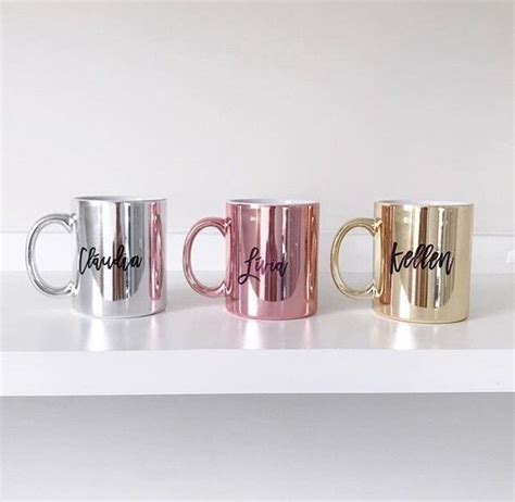 Three Metallic Coffee Mugs Sitting On Top Of A White Shelf