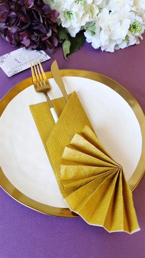 A White Plate Topped With Gold Napkins Next To Purple Table Cloth And