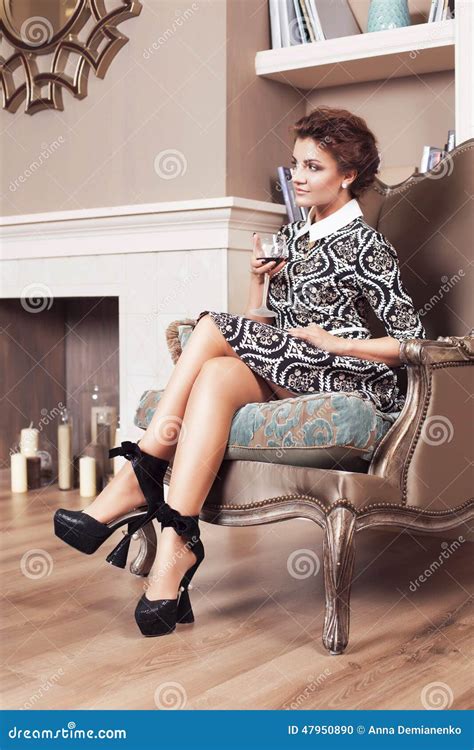 Beautiful Brunette Rich Saucy Woman In Elegant Dress Sitting On A Chair In A Room With Classic