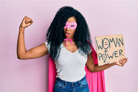 Middle Age African American Woman Wearing Super Hero Costume Holding Woman Power Banner In Shock