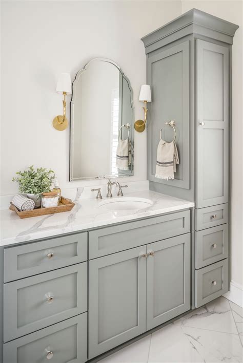 A Bathroom With Gray Cabinets And White Marble Counter Tops Gold