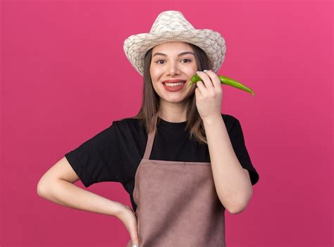Free Photo Smiling Pretty Caucasian Female Gardener Wearing Gardening Hat Holding Hot Pepper