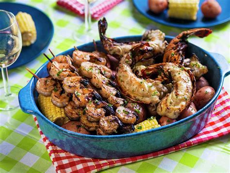 Grilled Prawn Kebabs And Lobster Tails On A Bed Of Corn Cobs And Red