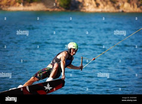 A Young Man Wearing A Helmut And Lifejacket Wakeboarding On A Lake