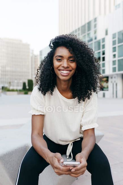 Portrait Of Smiling African American Woman Sitting On City Street With