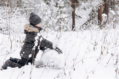 Criança feliz rolando grande bola de neve para boneco de neve na