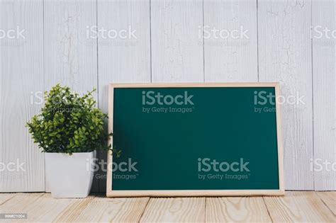 Blank Green Chalkborad With Wood Frame And Little Decorative Tree In White Vase On Wooden Table