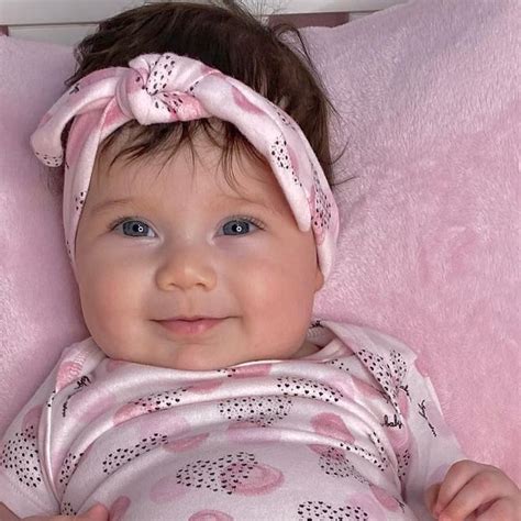 A Baby Laying On Top Of A Pink Blanket Wearing A Headband And Smiling