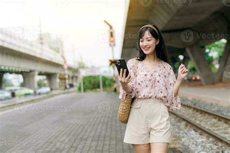 Asiático Joven Mujer Viajero Con Costura Cesta Utilizando Un Móvil Teléfono Junto A Ferrocarril