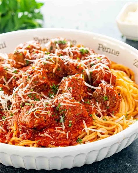 A White Bowl Full Of Spaghetti And Meatballs Garnished With Parmesan Cheese