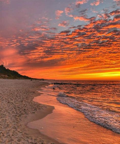 The Sun Is Setting At The Beach With People Walking On It