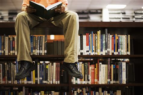 Man Reading Book and Sitting on Bookshelf in Library