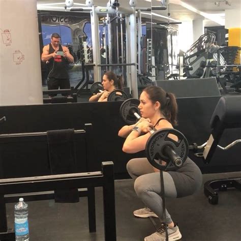 A Woman Squatting Down With A Barbell In Front Of Her And Another Man