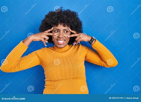 Black Woman With Curly Hair Standing Over Blue Background Doing Peace Symbol With Fingers Over