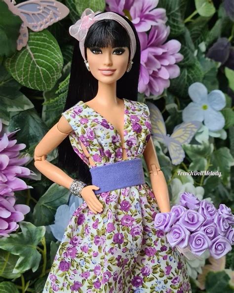 A Barbie Doll Holding A Bouquet Of Purple Flowers In Front Of Some