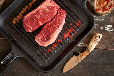 Two Fresh Juicy New York Steaks On A Grill Pan With Sprinkled Spices