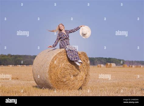 Une jeune fille blonde aux cheveux longs dans un chapeau blanc se repose et pose près des gerbes