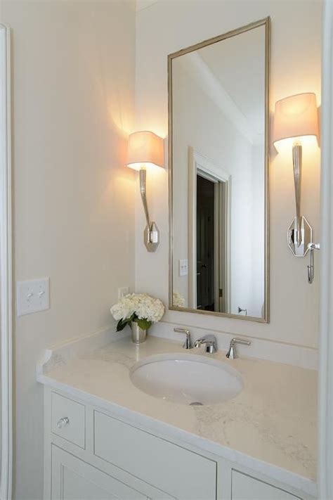 Ruhlmann Single Sconces Flank A Tall Metal Mirror Fixed On A White Wall