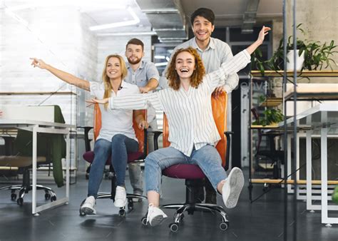 Happy Colleagues Having Fun At Workplace Making Office Chair Race