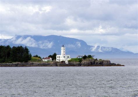 A Lighthouse On An Island In The Middle Of Water With Mountains In The