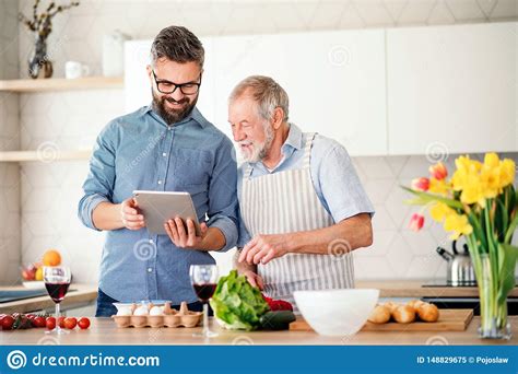 Adult Hipster Son And Senior Father Indoors In Kitchen At Home Using