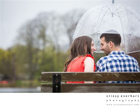 Rainy Engagement Pic Of Couple On Bench Under Umbrella