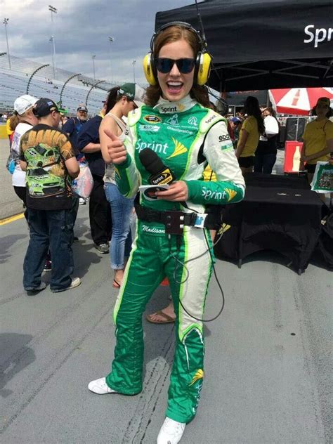 A Woman With Headphones On Standing In Front Of A Race Car And Giving