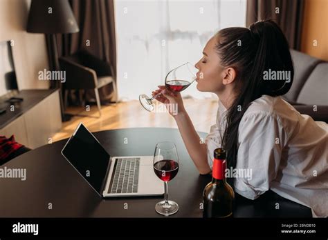 Side View Of Young Woman Drinking Red Wine Near Laptop With Blank