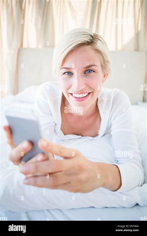 Smiling Blonde Woman Lying On The Bed And Texting With Her Mobile Phone Stock Photo Alamy