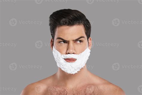 Ready To Shave Confused Young Man With Foam All Over His Face Looking Away While Standing