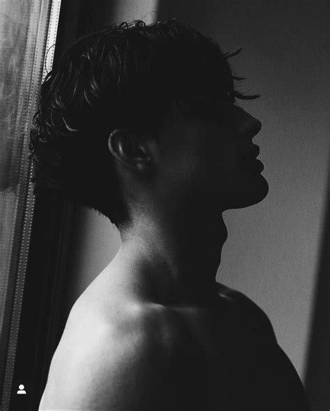 A Black And White Photo Of A Shirtless Man Looking Out The Window At