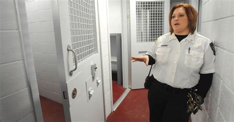 A Woman In Uniform Standing Next To A Wall With Jail Cell Doors On Both Sides